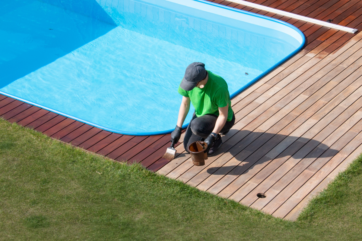 야외 수영장의 목재 바닥에 보호제 칠하는 사람 사진